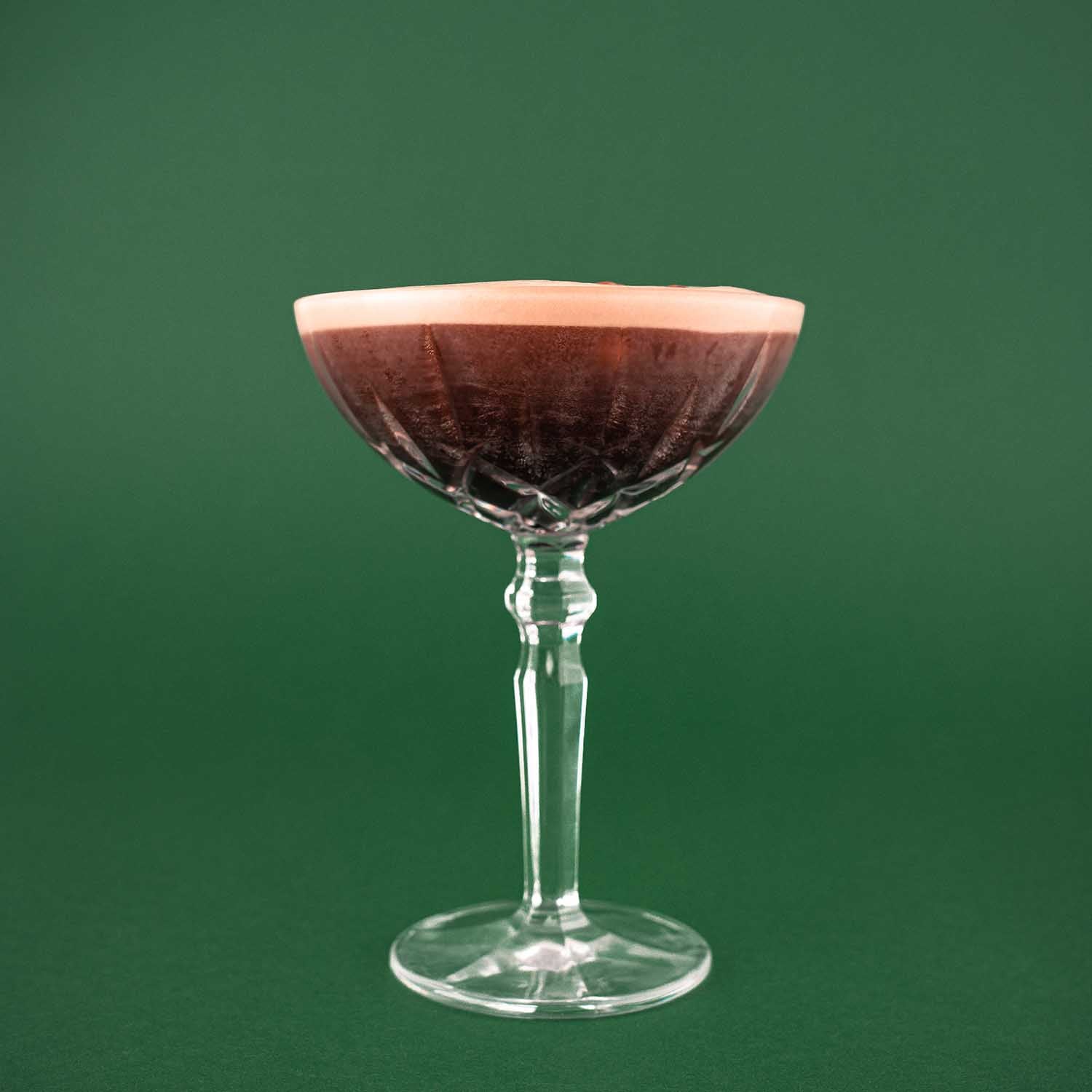 Hazellujah Nusslikör Espresso martini, Espresso Cocktail im Martini-Glas mit Schaumkrone, dekoriert mit Kaffeebohnen, vor dunkelgrünem Hintergrund