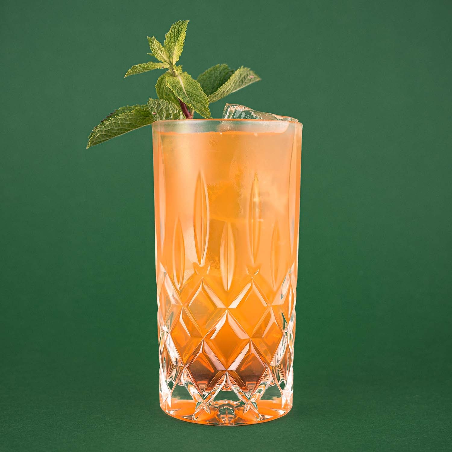 Hazzelujah Nusslikör Cocktail im Longdrinkglas vor einem dunkelgrünen Hintergrund, dekoriert mit Minzblättern