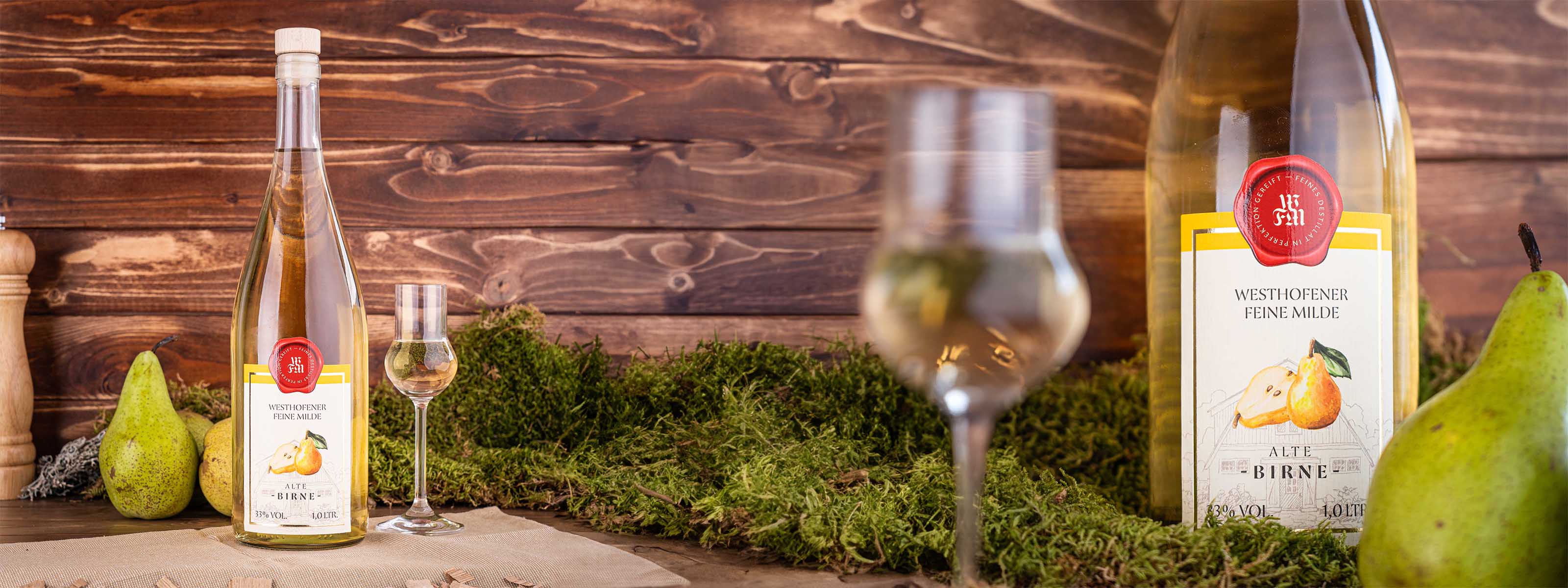 Westhofener Feine Milde Alte Birne und Nosing-Glas im Vordergrund, zwischen frischen Birnen, Moos und dunkle Holzlatten im Hintergrund