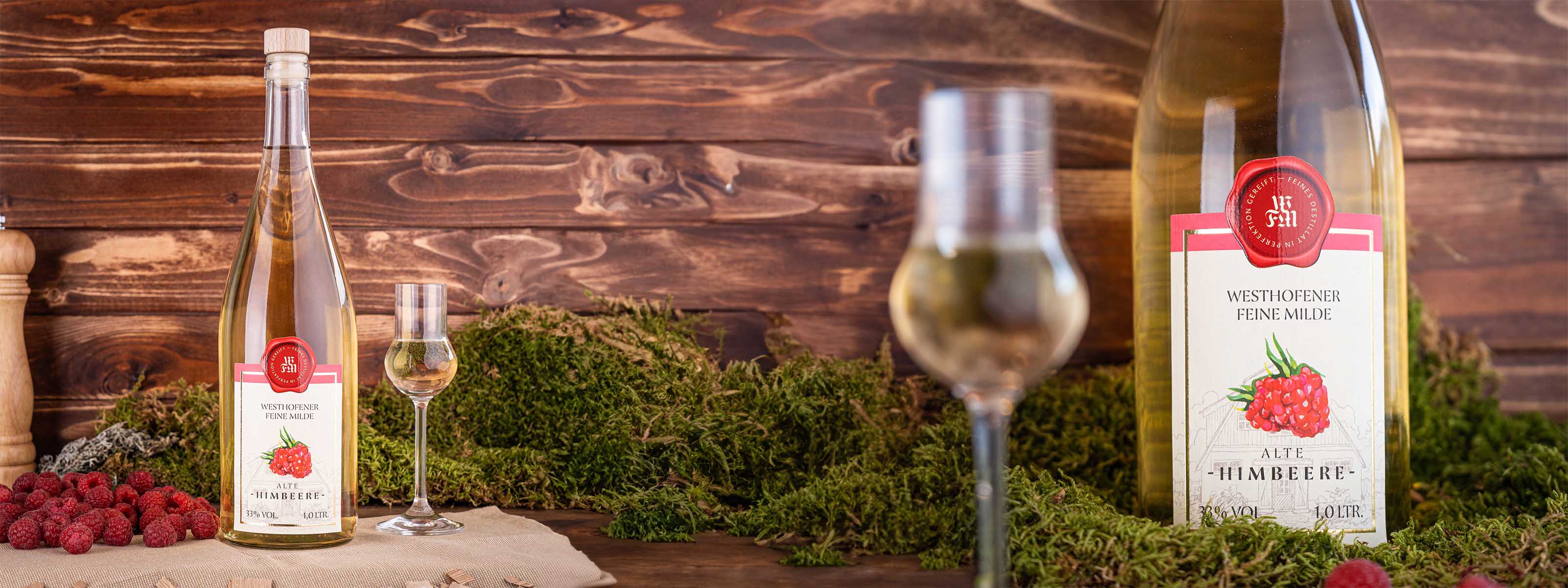 Westhofener Feine Milde alte Himbeere, Flasche und Nosing-Glas im Vordergrund zwischen frischen Himbeeren, Moos und dunkle Holzlatten im Hintergrund