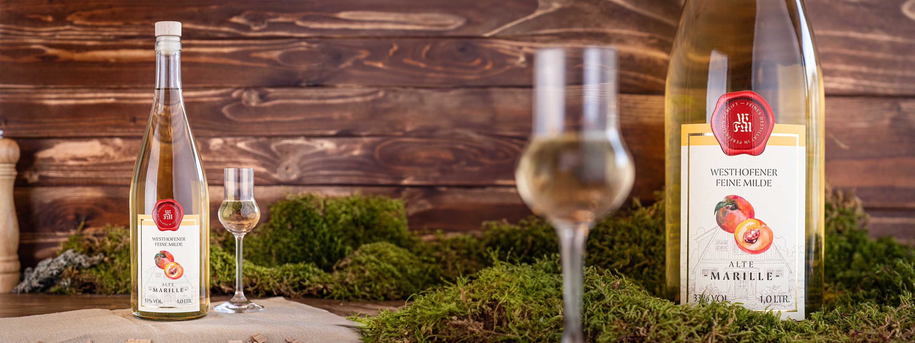 Westhofener Feine Milde Alte Marille, Nosing-Glas und Flasche im Vordergrund, Moos und dunkle Holzlatten im Hintergrund