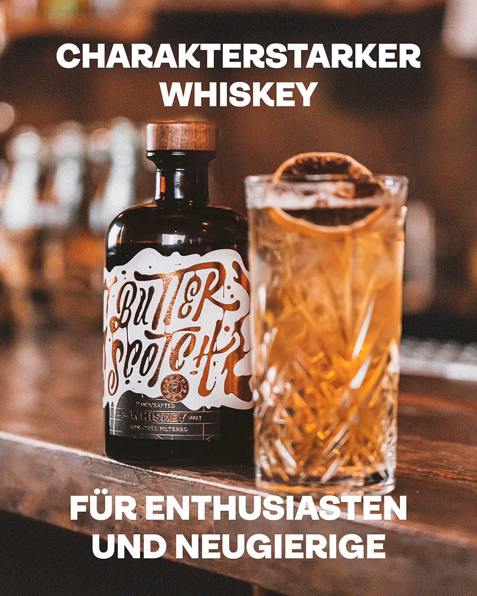 Charakterstarker Whiskey, Für Enthusiasten und Neugierige, Butterscotch Whiskey und Longdrink im geschliffenen Glas im Vordergrund, auf dunklem Holztresen in gemütlichem Bar-Ambiente