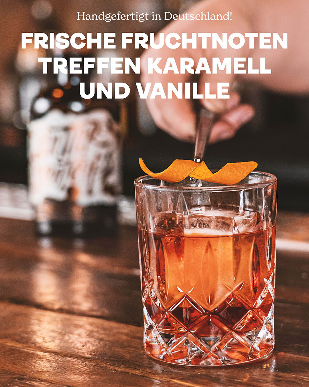 Butterscotch Single Malt Whiskey, Handgefertigt in Deutschland, Frische Fruchtnoten treffen Karamell und Vanille, Negroni-Drink im Vordergrund, dekoriert mit Orangenzeste, Butterscotch Whiskey-Flasche im Hintergrund auf dunklem Bartresen 