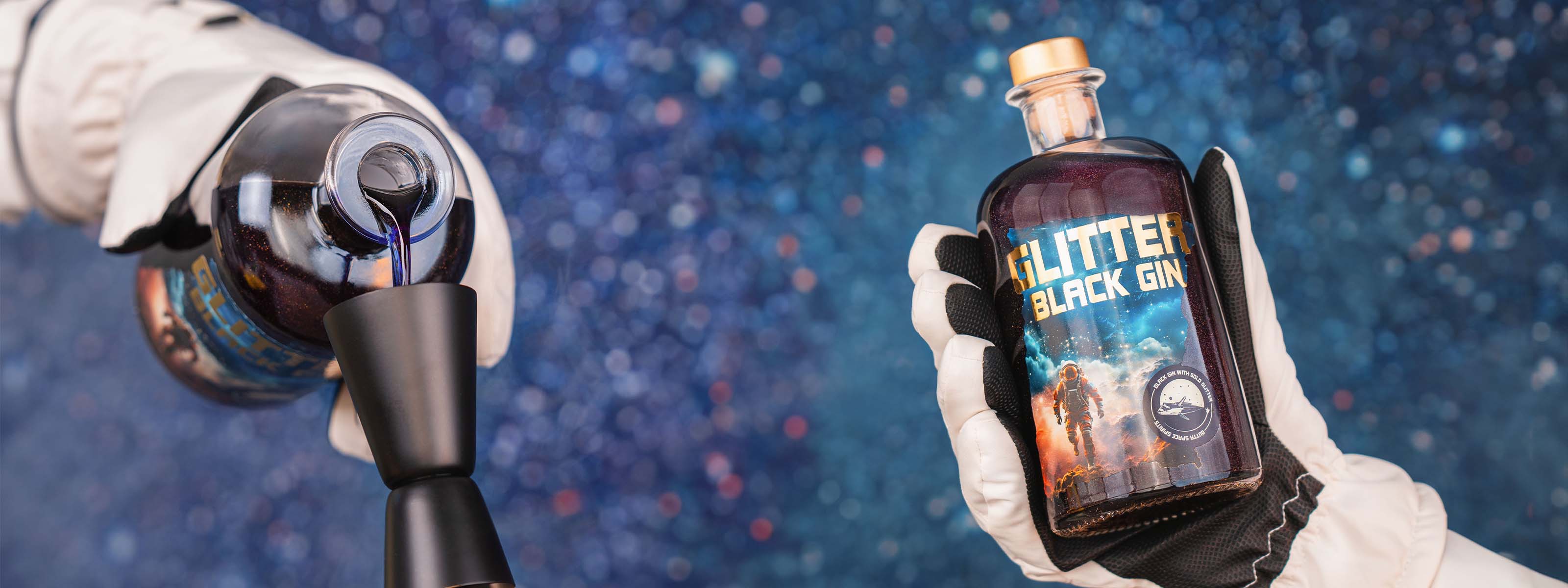 Glitter Black Gin Flasche mit essbarem Glitzer im Vordergrund, blauer Gin wird eingegossen in einen mattschwarzen Messbecher, vor einem dunklen Sternenhimmel-Hintergund