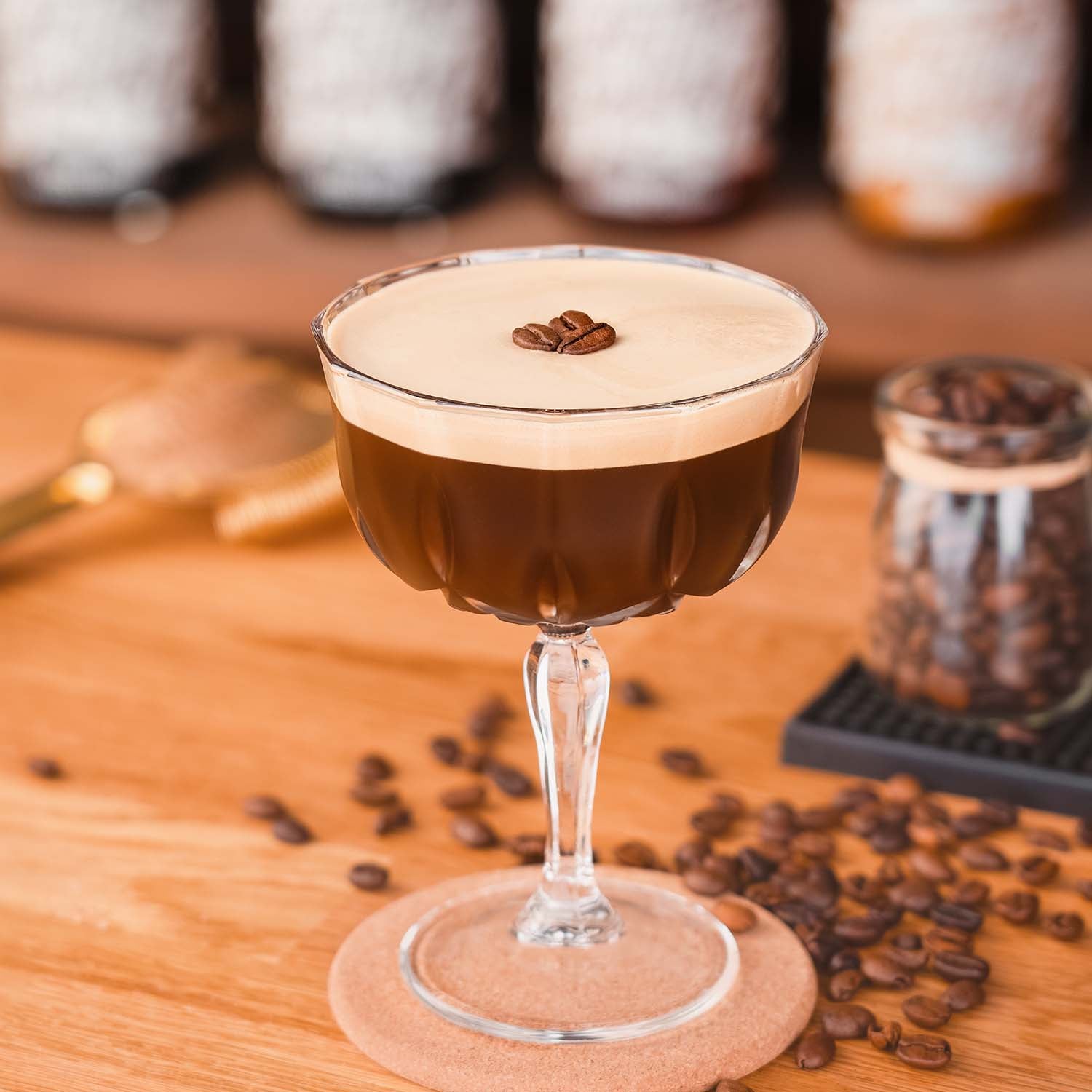 Butterscotch Espresso Martini Cocktail, Espresso Martini im Glas, dekoriert mit Kaffeebohnen, Kaffeebohnen und Butterscotch Flaschen als Dekoration im Hintergrund