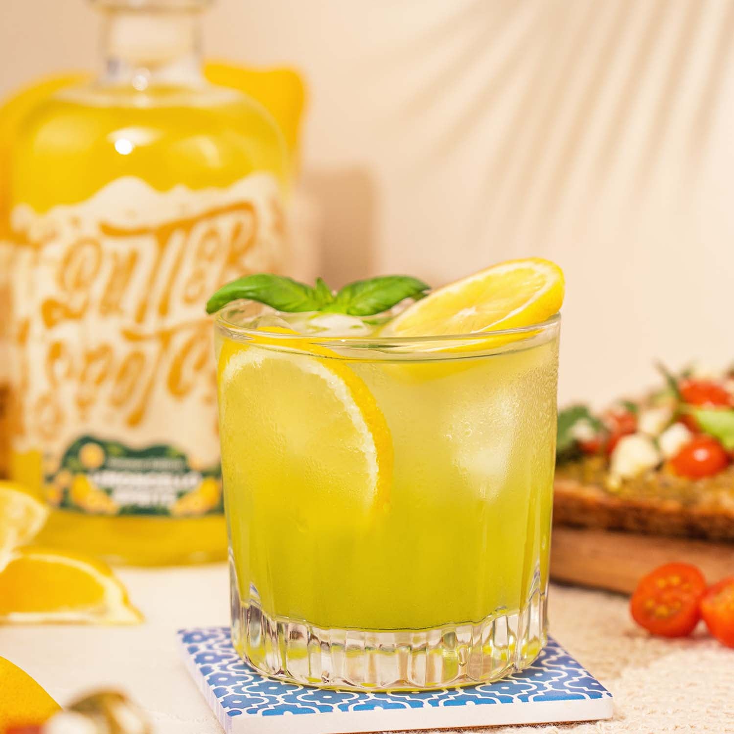 Basil Smash Cocktail mit Limoncello Spritz Likör, Gelber Cocktail mit Zitronenscheiben und Basilikumblättern garniert, Flasche und Obst im Hintergrund