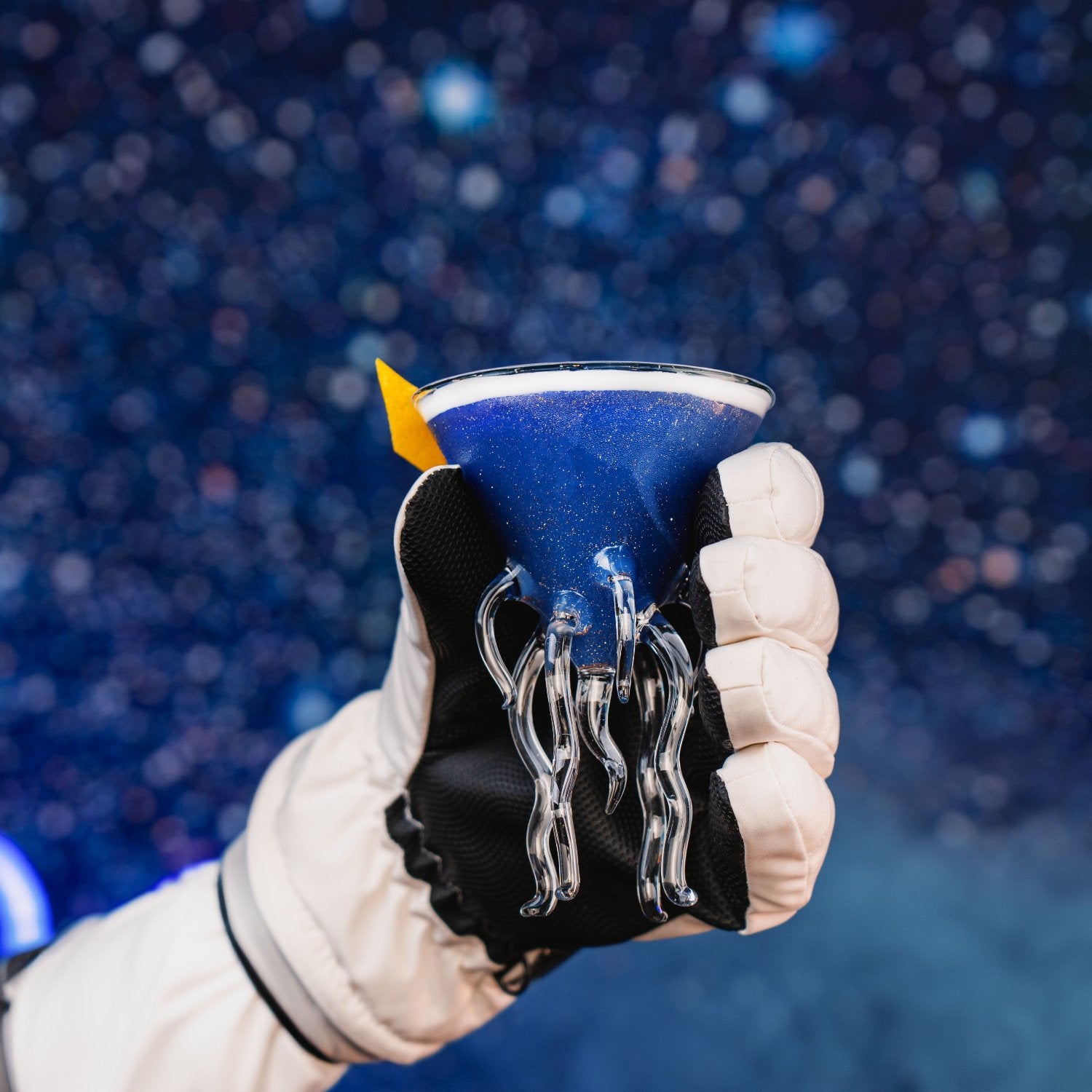 Glitter Black Gin - Blue Lady Cocktail, ein schimmernder blauer Glitzer-Cocktail, serviert in einem Space-Martini-Glas, das in der reflektierenden Scheibe eines Astronautenhelms erscheint.