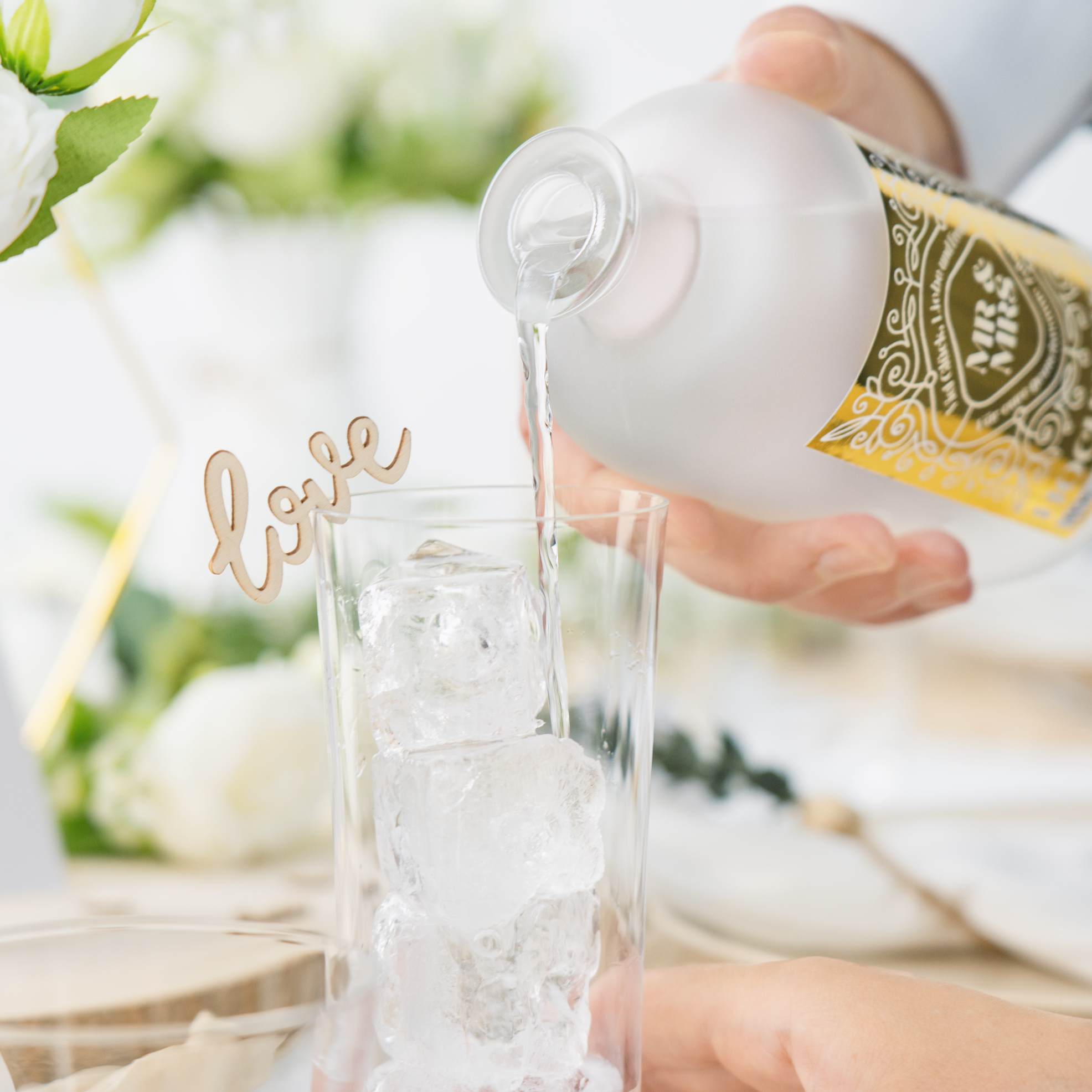 Klassischer Zitrus-Wacholder Gin mit gold glänzendem Etikett, individuell personalisierbar & ideal als Geschenk zur Hochzeit, Gin wird in ein Glas mit Eis gegeben