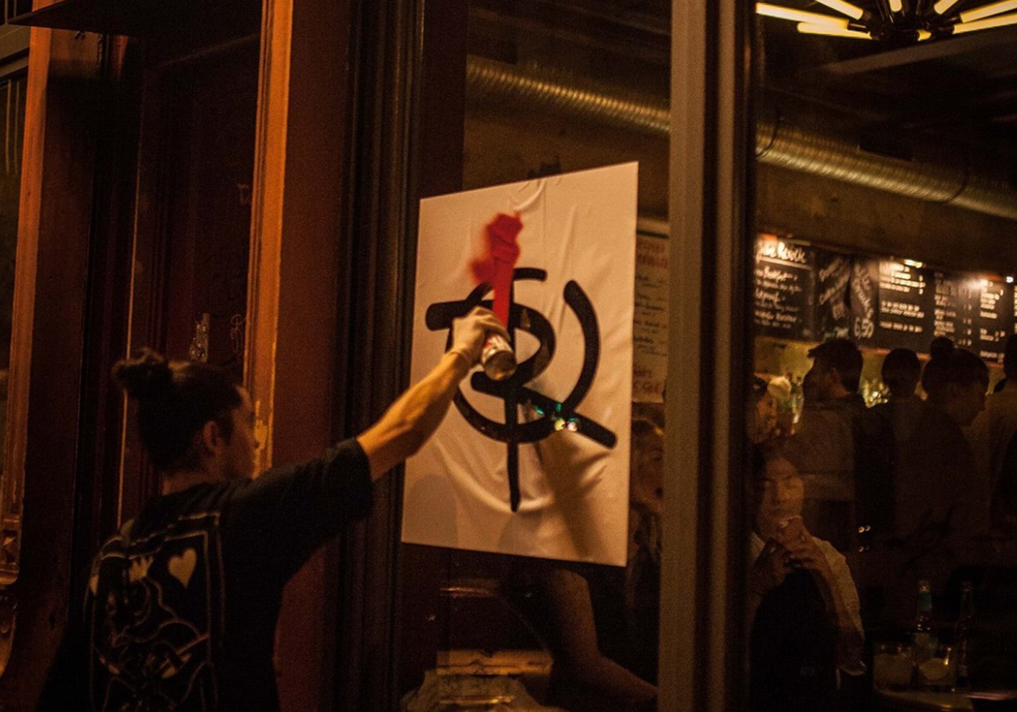 Revolte Rum Logo am Fenster einer Bar wird mit roter Farbe besprüht, Menschen im Hintergrund in einer Bar-Atmosphäre